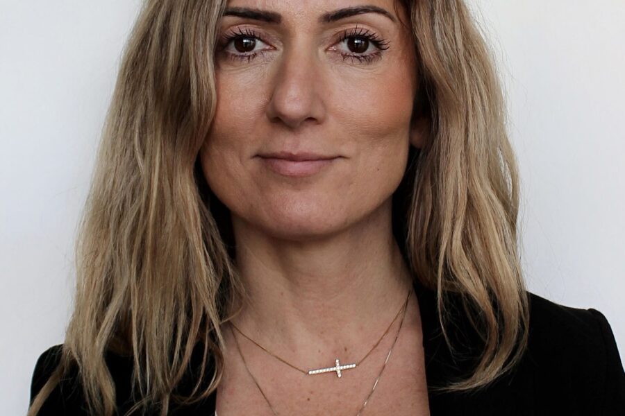 Portrait of AKG CEO with long brown hair and black jacket against light background.