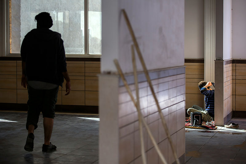 Person går ensam genom en tom byggnad medan en annan arbetar i ett avskilt rum, vilket symboliserar socialt utanförskap.